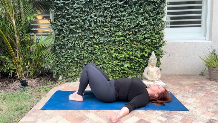 woman practicing yoga outdoors on a mat laying on her back with knees bent