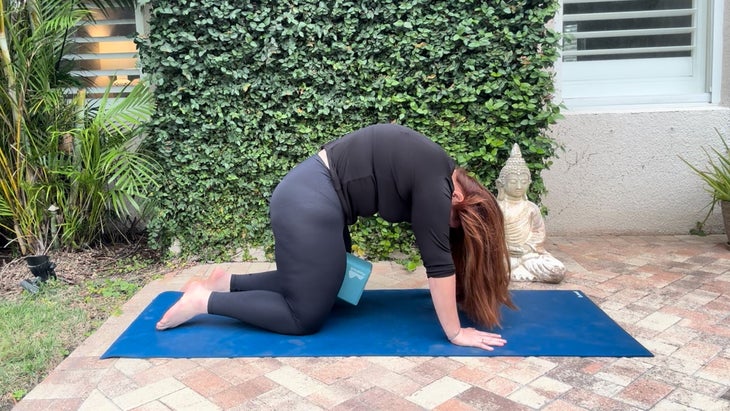 woman practicing yoga outdoors on a mat in cat pose