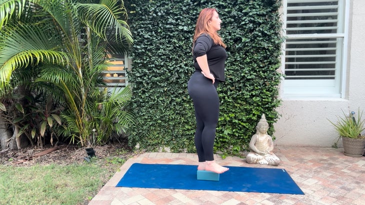 woman practicing yoga outdoors on a mat with a block