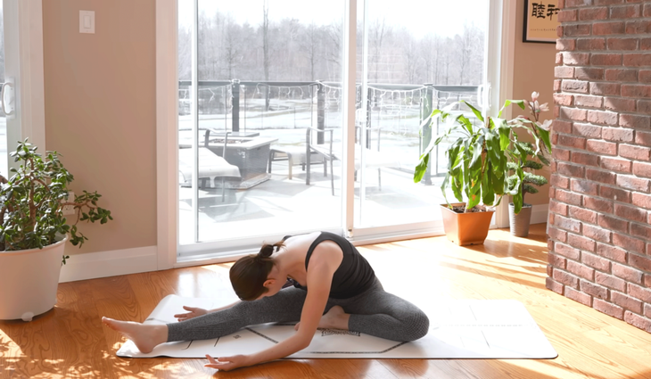 Woman sitting on a yoga mat in Head to Knee pose, or Janu Sirsasana, while practicing stretches for sleep