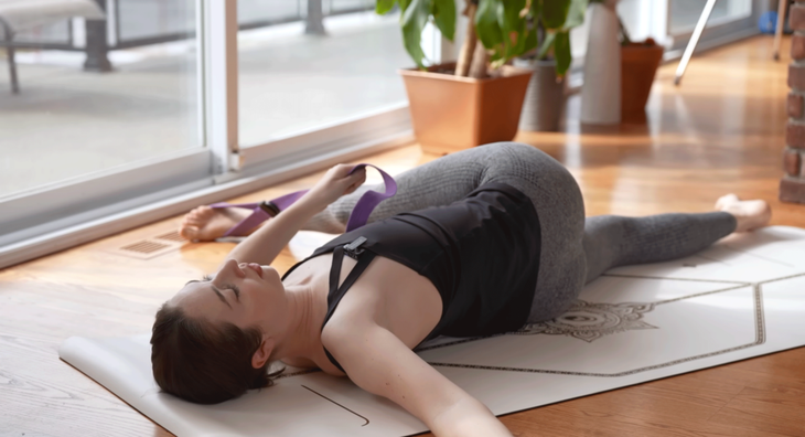 Woman reclining on a yoga mat in a twist with her leg reaching across her body.