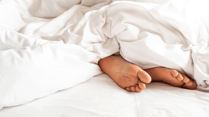 Woman lying in bed asleep with her feet sticking out from beneath a white comforter