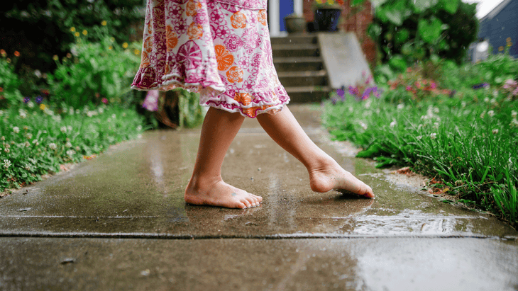 Little girl wearing a colorful pink dress while barefoot on a wet sidewalk after the rain while practicing ways to be mindful