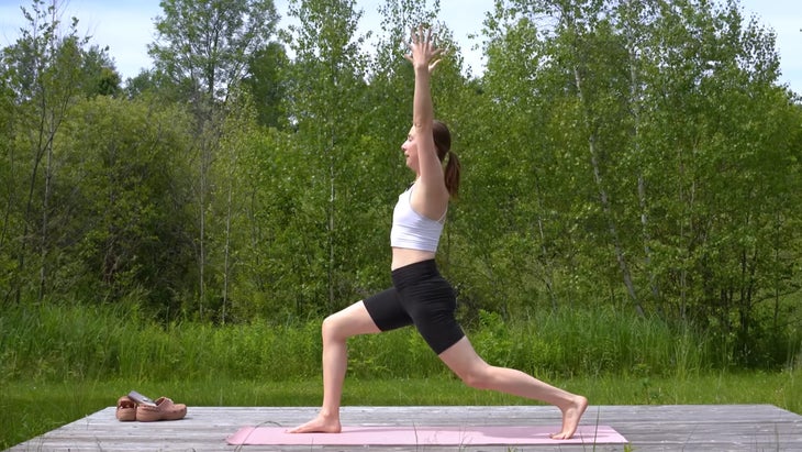 woman outdoors on a yoga mat practicing high lunge pose