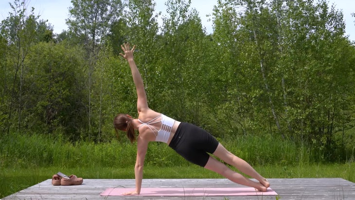 woman outdoors on a yoga mat in a side plank pose