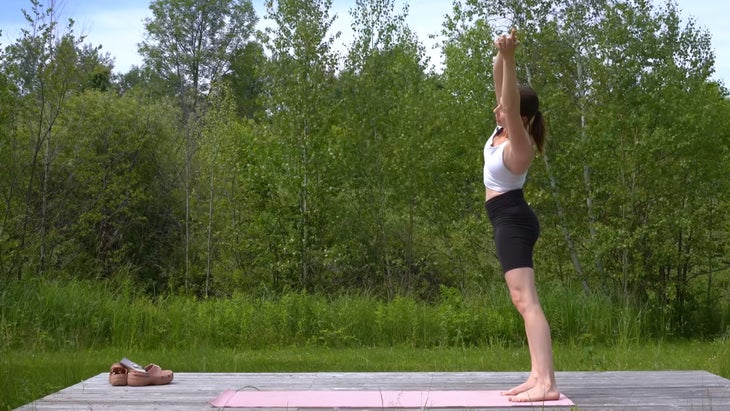 woman outdoors on a yoga mat standing with her arms outstretched over her head