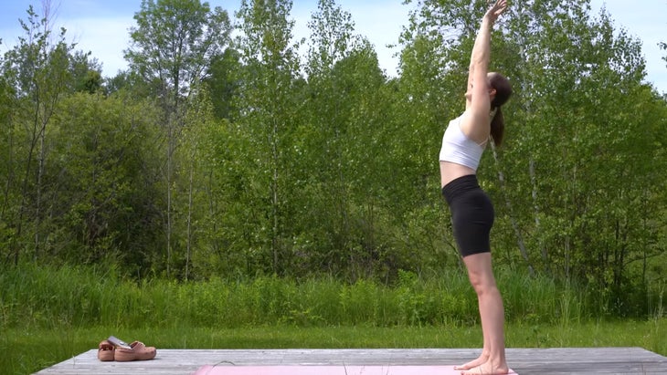 woman outdoors on a yoga mat preparing to do a forward bend