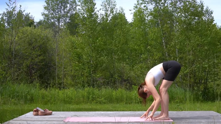 woman outdoors on a yoga mat prating a standing forward bend