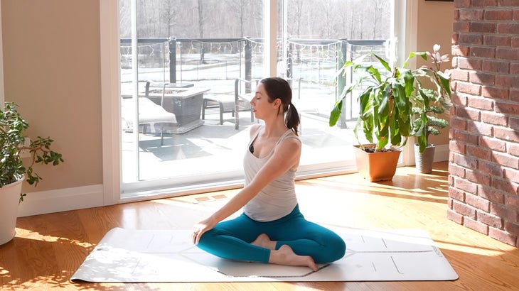 Woman on a yoga mat practicing a 15-minute yoga flow without using her hands twisting to her right