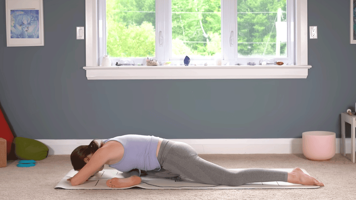 Yoga With Kassandra practicing a 20-minute yoga class on a yoga mat placed on carpet with a window and trees in the background