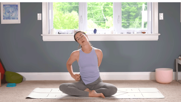 Woman sitting cross-legged on a yoga mat leaning her head to the side