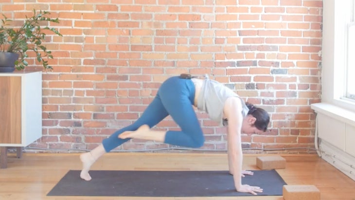 Woman on a yoga mat learning how to step from the back of the yoga mat to the front