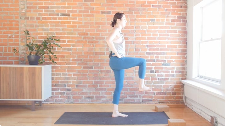 Woman standing on a yoga mat placed on a wooden floor with a brick background