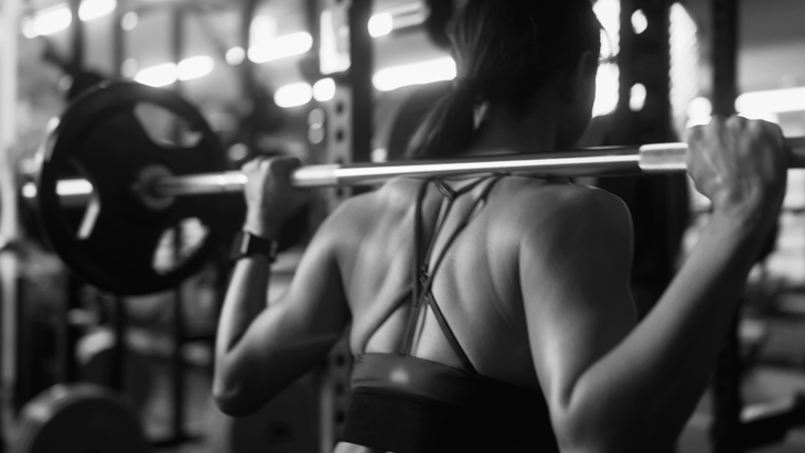 Woman with a barbell on her shoulders practicing a squat