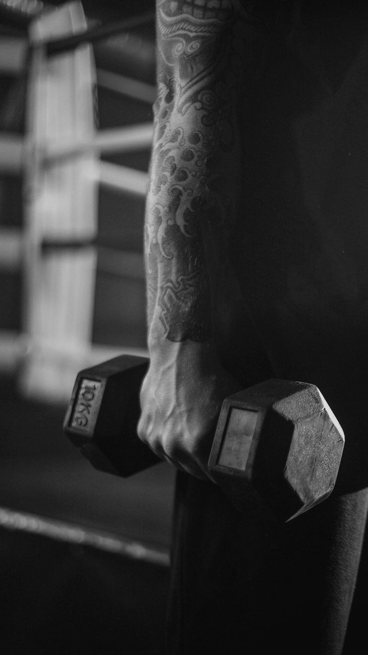 Man with tattoos lifting a dumbbell in a gym because he practices yoga and strength training