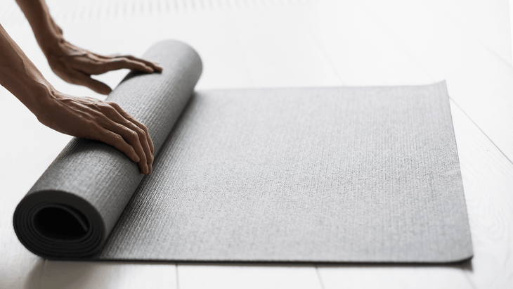 Woman unrolling a yoga mat on a wood floor