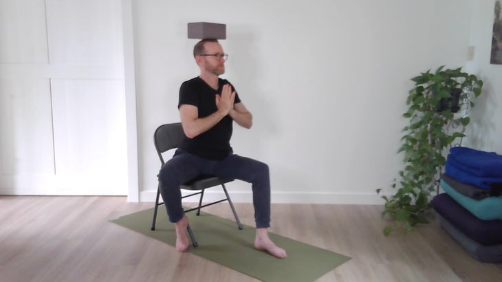 man practicing yoga positions on a chair