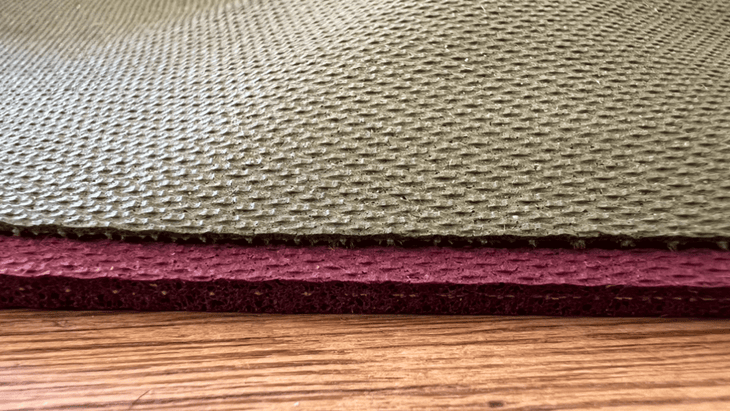 Two Jade yoga mats--a standard mat and a travel mat--stacked on top of one another on a hardwood floor to show the difference in thickness