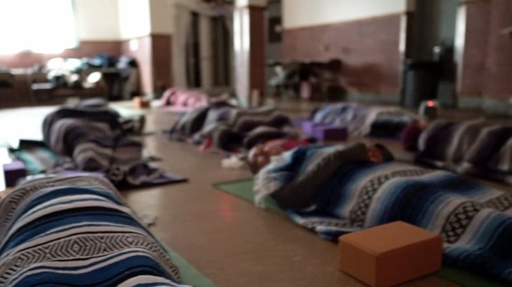 Una clase de estudiantes de yoga acostados en sus colchonetas en Savasana.