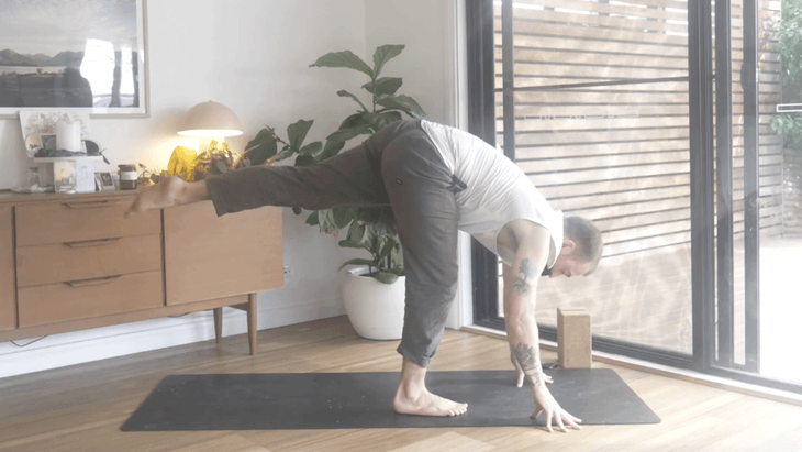 Man practicing Standing Splits with his left leg lifted behind him while standing on a yoga mat