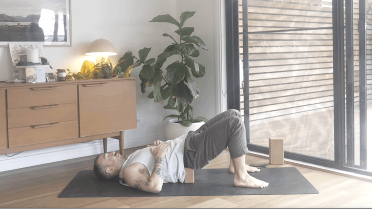 Man on a yoga mat with a block beneath his lower back to help stretch and lengthen the muscles along the lumbar spine