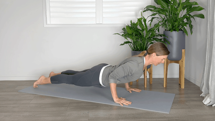 Woman lowering herself to the mat in Chaturanga with yoga strap around her lower arms