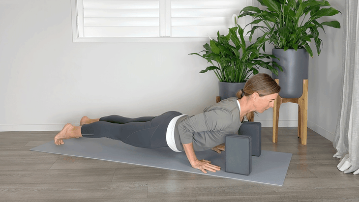 Woman practicing Chaturanga on a yoga mat with blocks beneath her shoulders to prevent them from rounding