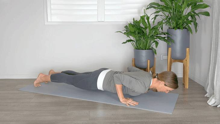 Woman practicing Chaturanga on a yoga mat with her shoulders rounded forward