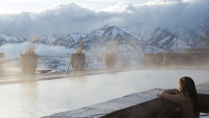 Woman in an infinity pool overlooking snow-covered mountains