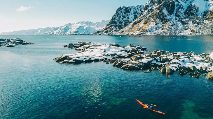 a kayaker in a bay with snowy mountains in the background