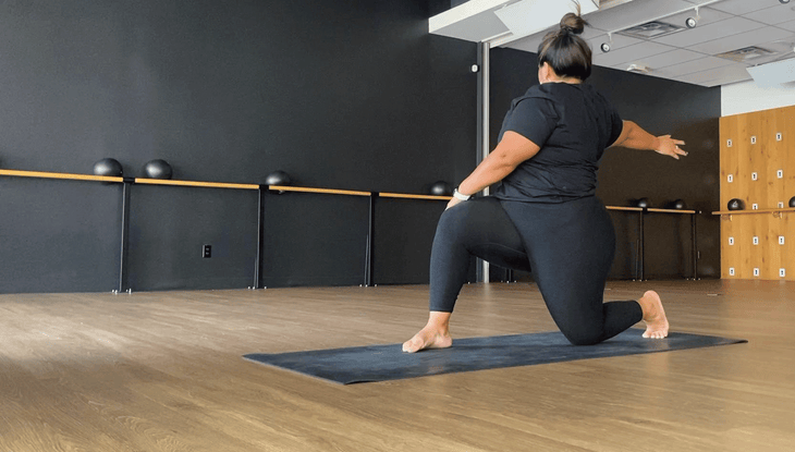 Woman on a yoga mat in a low lunge twist with her back knee down