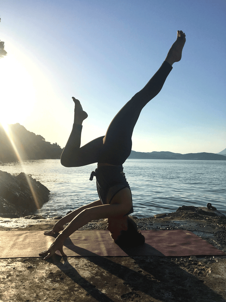 Restaurant manager Jenny Schubert practicing yoga on rocks overlooking water.