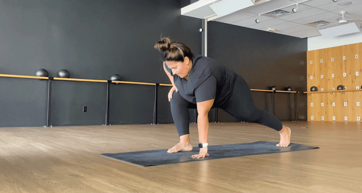 Teacher practicing low lunge with the right foot forward on a yoga mat in a studio