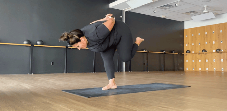 Yoga teacher on a black mat on a hardwood floor practicing shiva squat