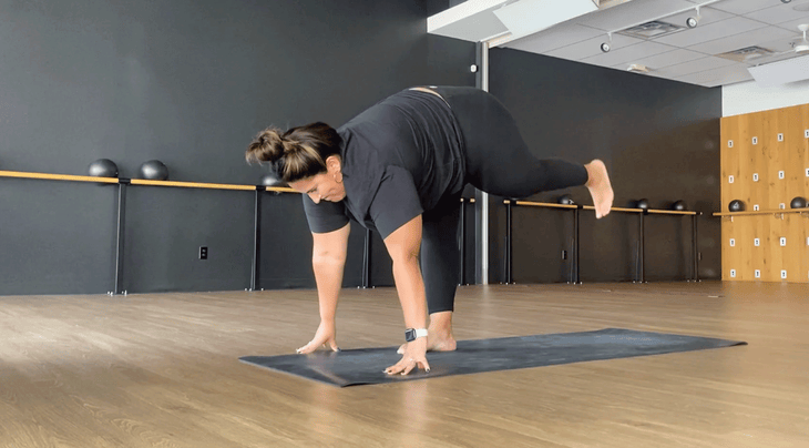 Yoga teacher practicing Standing L on a yoga mat in a studio