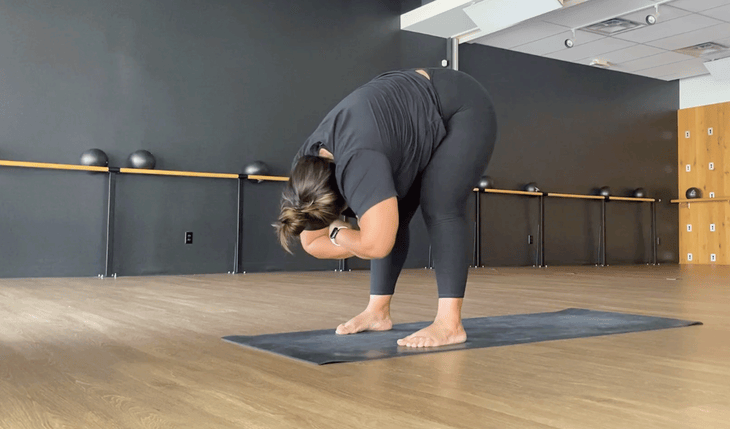 Yoga teacher standing in a forward bend on a yoga mat.