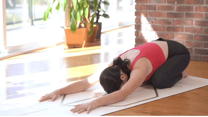 woman in child's pose or balasana on a yoga mat