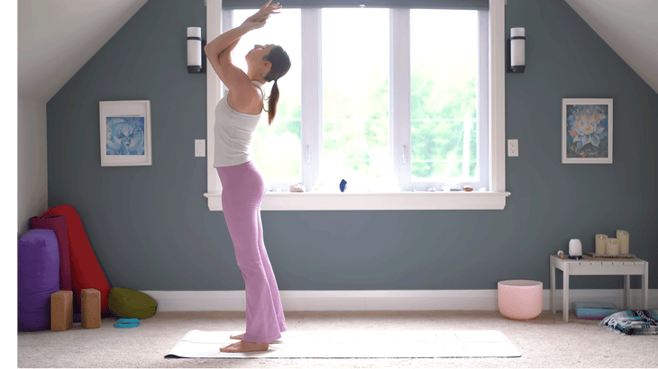 Woman standing with her elbows crossed in Eagle Arms while leaning backward into a slight backbend