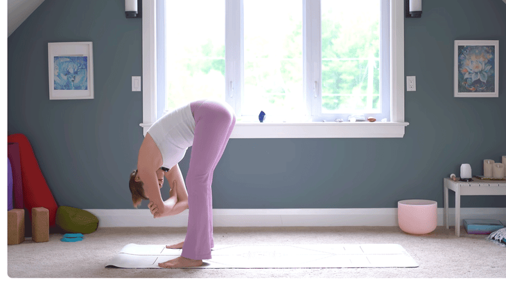 Woman standing at the front of the mat leaning forward while holding onto opposite elbows