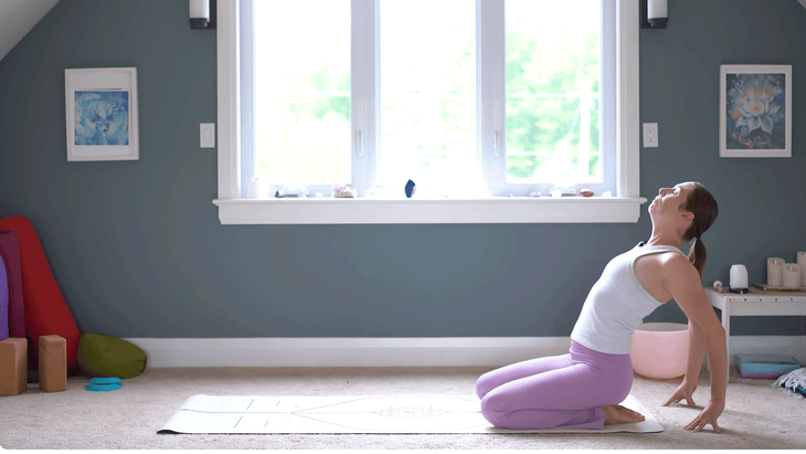 Woman kneeling on a yoga mat with her fingertaps behind her and her chest lifted and leaning back