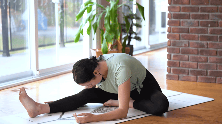 Woman sitting and leaning forward over a straight right leg while practicing yoga for lower back pain