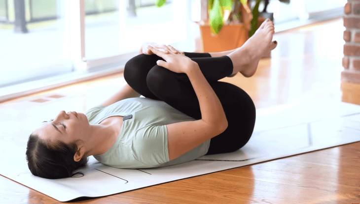 Woman lying on a yoga mat drawing her knees to chest while practicing yoga for lower back pain