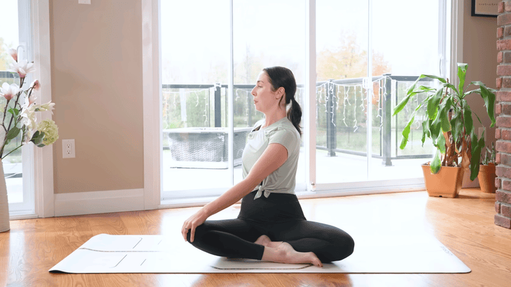 Woman sitting on a yoga mat twisting to her right for lower back pain relief