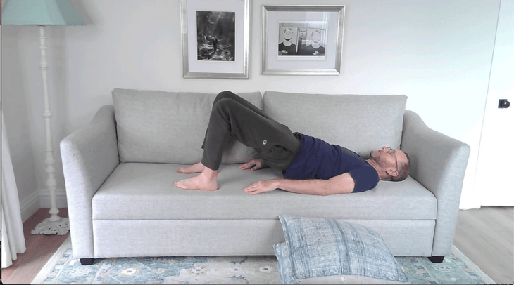 Man lying on his back on a couch practicing Bridge Pose