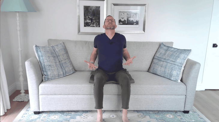 Man sitting on the edge of a couch with his back arched in seated Cow Pose