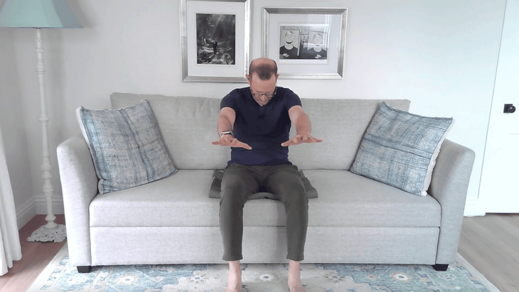 Man practicing couch yoga by sitting on a couch and rounding his back