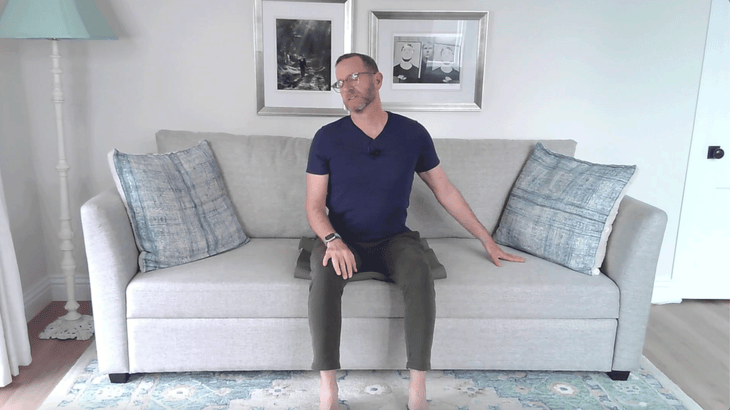 Man sitting on couch leaning away from his left side for a stretch