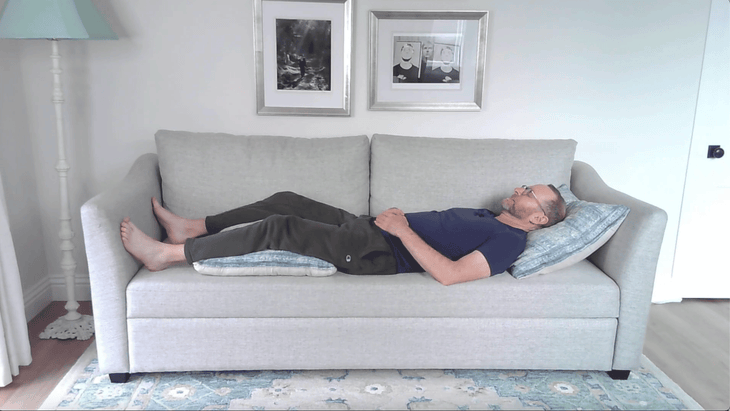 Man lying on a couch with a pillow under his head and pillows beneath his legs