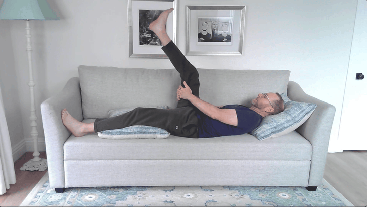 Man lying on a couch with his right leg lifted in a hamstring stretch