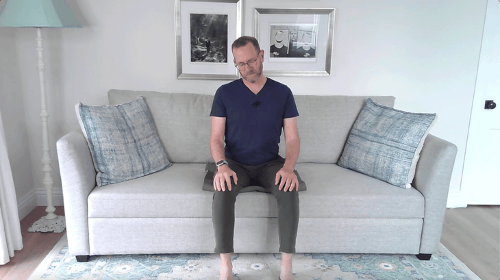 Man sitting on a couch in a living room leaning his head to his right for a neck stretch